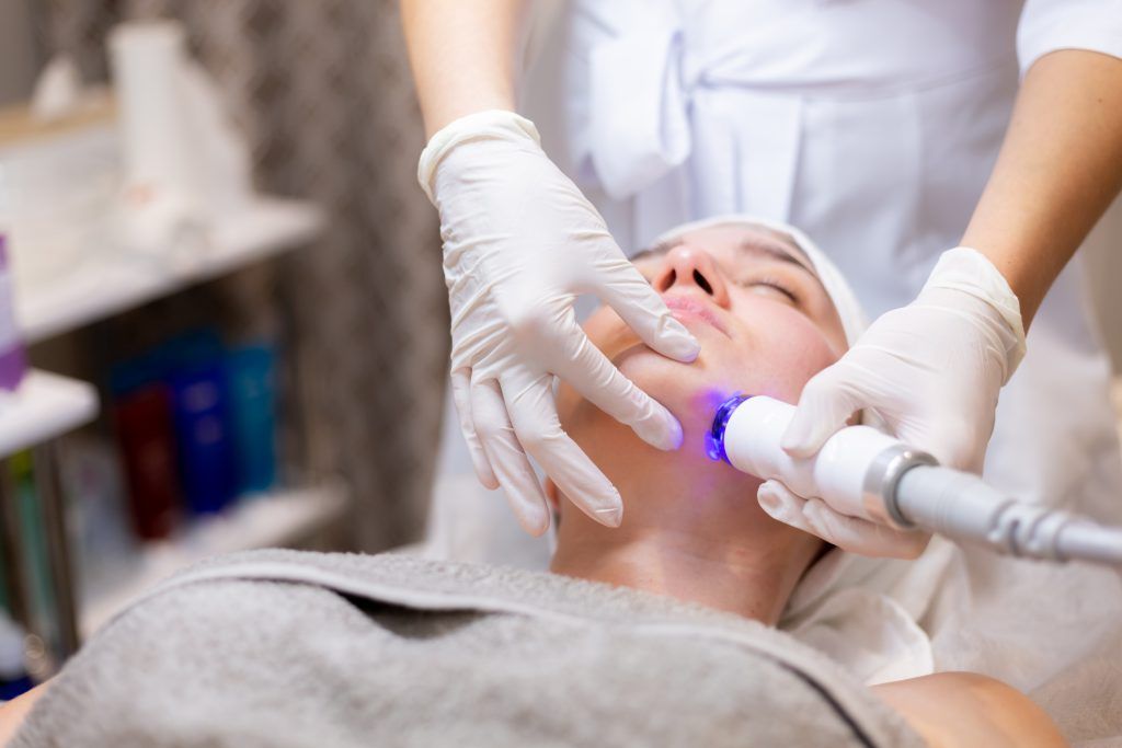 A young beautiful girl lies on the beautician's table and receives procedures with a professional apparatus for skin rejuvenation and moisturizing